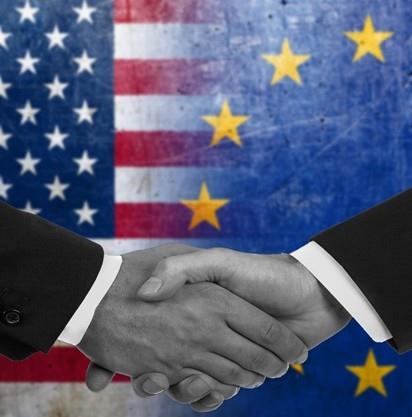 Due mani che si stringono su uno sfondo con le bandiere degli Stati Uniti e dell'Unione Europea