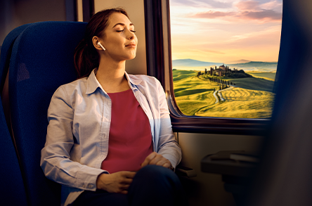 Una persona seduta su un treno ammira un paesaggio pittoresco con dolci colline e un villaggio lontano sotto un cielo al tramonto.